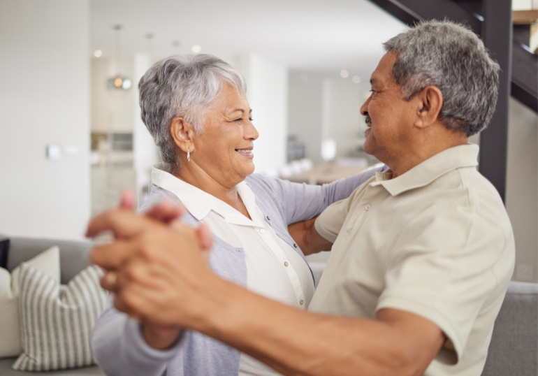 Elderly man and woman dancing with each other in the living room. Not actual patients.